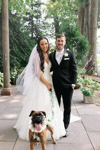 Bride and groom pose with their flower dog before their wedding cweremony.