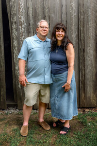 Grandparents standing together in front of rustic wooden barn during extended family session in New Bern North Carolina