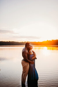 a women standing with her back to her husband in an embrace in a lake with a sunset behind her