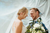 Bride and groom smiling under flowing veil during intimate wedding day portrait in Colorado.