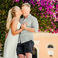 A smiling bride holding a pastel floral bouquet while being embraced by the groom outdoors, captured in a joyful and romantic wedding moment.