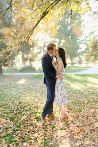 Couple kisses under a tree amid autumn foliage.