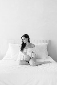 Black and white studio portrait of a pregnant woman in white shirt on bed, fine art maternity photographer Miami