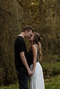 Engaged couple standing forehead to forehead under a willow tree during a romantic Maine engagement photography session