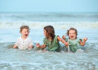 Three young siblings laughing and splashing in the shallow ocean waves during a beach child portrait session. (Photographed by Nature's Child Photography)