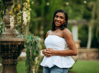 Senior portrait at Bella Sera Gardens in Loxley, Alabama — sitting on a bridge rail with a pond
reflecting behind her.
