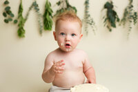 baby sitting up with cake frosting on his face during milestone portrait session at CG Photography Los Angeles