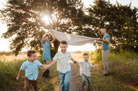 children run under a blanket during their family photo session at erwin park in mckinney,texas.