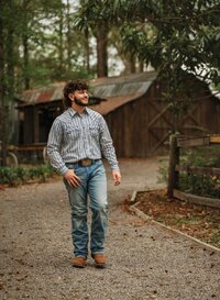 Senior portrait at Circle B Lake in Wilmer, Alabama — walking down a gravel road, looking to
the side with the old barn behind him.