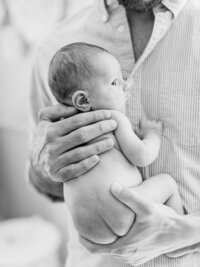 Black and white portrait of a father holding his awake newborn baby during an in-home lifestyle newborn session.