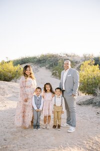 The Collins family posing together in the Las Vegas desert during golden hour, with parents and three children smiling in a natural outdoor setting for a warm, candid family portrait session.