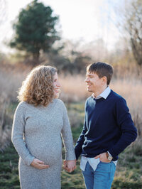 Man and woman walking and looking at each other at Magnuson Park grassy fields during their maternity session.
