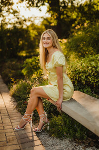 A young woman from Arrowhead High School sits on a concrete bench at Waukesha's Retzer Nature Center wearing a yellow sundress.