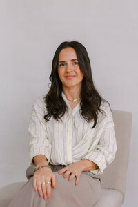 Woman sitting on a chair on a white backdrop and with her hands softly in her lap, while posing for her bay area branding photography photoshoot