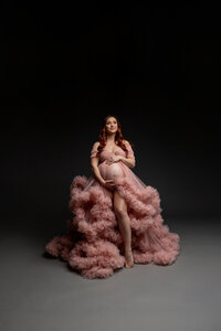 Pregnant woman wearing a dramatic pink ruffle maternity gown during a fine art studio maternity photography session by Kaitlyn Dawn Photography.
