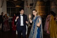 A couple dressed in formal attire dancing at a festive event, surrounded by guests in colorful dresses.