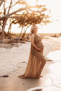 Folly Beach Maternity Photographer -- Pregnant woman poses for Maternity Photos at the Lighthouse Inlet Heritage Preserve on Folly Beach with iconic views of the Morris Island Lighthouse in the distance.