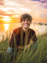 High school senior boy smiling in tall coastal grass during sunset in Eastern North Carolina