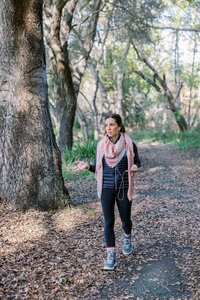 Woman walking through wooded area and taking a work phone call on her headphones