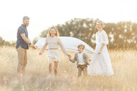 A family of 4 standing in a grassy field at a Fort Worth TX park as they play with their children for family photos.