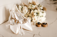 a close up detail shot of the brides shoes, rings, and flowers in the bridal suite.