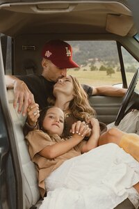 A husband kisses his wife on the forehead with their daughter snuggling in close inside the cabin of their vintage truck during family photo session in Colorado.