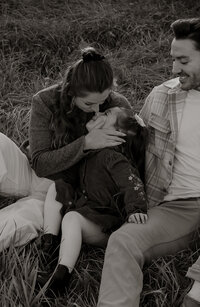 A sweet, candid moment of a mom giving her daughter a kiss on the nose while they cuddle in the grass. A warm, intimate family photography capturing genuine connection.