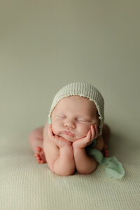 Sleeping newborn baby wearing a knit bonnet and posed on a soft green blanket during a studio session with newborn photographer Kaitlyn Dawn Photography.