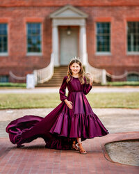 Child in a rich purple gown posing in front of a historic brick home in New Bern