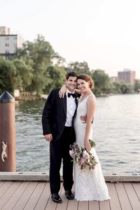 Bride and groom embrace with wedding bouquet on dock