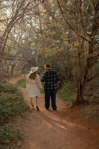 Couple walking hand-in-hand along a wooded trail during their Lover's Knoll engagement session