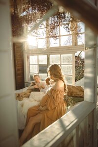 Pregnant mother sitting on a bed wearing a yellow dress inside a greenhouse