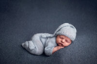 Sleeping newborn in light blue knit outfit and hat on dark blue backdrop, taken at a professional photo studio near Brookfield and Waukesha