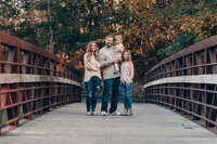 Family of four in coordinated blush and neutral outfits standing on a wooden bridge during a Cleveland family photography session