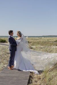 Brides veil blows in the wind with ocean behind her during wedding on Nantucket.