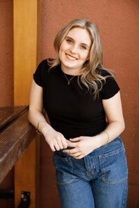 Smiling high school senior girl leaning against a wooden railing in warm golden light, senior portrait session by Kaitlyn Dawn Photography.
