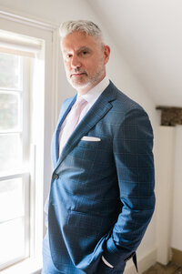 Groom stands in front of a sun lit window
