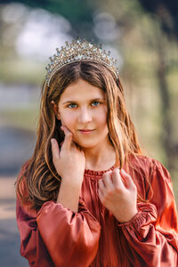 Close up portrait of a child wearing a crown and dusty pink dress in soft evening light