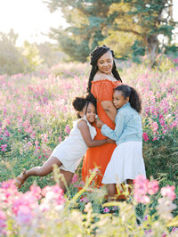 Two sisters hugging their pregnant mom in a sweet pea meadow in Discovery Park in Seattle