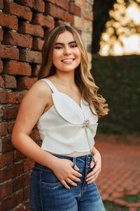 Senior portrait in downtown Mobile, Alabama — headshot with a greenery wall in the background and a red brick wall.
