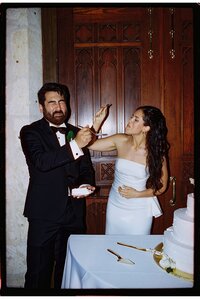 A couple feeding each other cake on their wedding day the bride tries shoving it into the groom's mouth and he makes a funny face. Shot on film with flash in San Antonio.