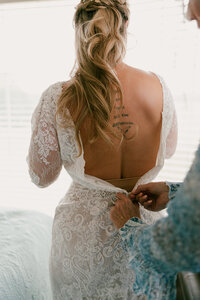 A person helping someone zip on their wedding dress