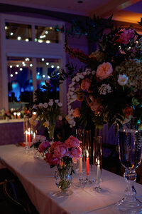 Romantic wedding reception table adorned with vibrant floral centerpieces, including pink roses and cascading greenery, surrounded by glowing candlelight at Burritt on the Mountain.