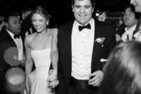 Black and white photo of Callie and Hayes walking hand-in-hand, smiling joyfully, during their Burritt on the Mountain wedding celebration.