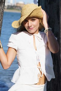 Young woman in a white top and a straw hat at the edge of the water smiling for a photo