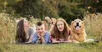 Jacksonville, FL portrait session capturing Three children lying in tall grass laughing and making silly faces beside their smiling golden retriever during a golden hour outdoor family in the Midwest countryside.