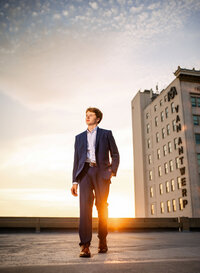 Senior portrait in downtown Mobile, Alabama— walking in his blue dress suit with the sunset backlighting him.