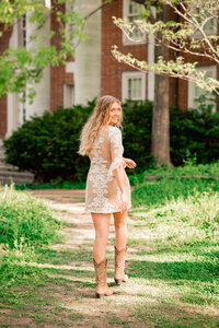 College senior wearing a lace dress and smiling over her shoulder as she walks across the Vanderbilt campus