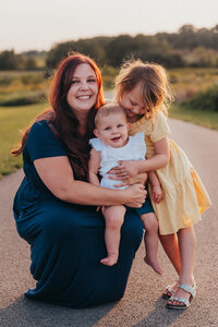 Mother smiling while holding her baby and young daughter outdoors during a Cleveland family photography session