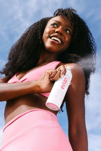 Model in pink activewear misting against a bright blue sky, shot from below
